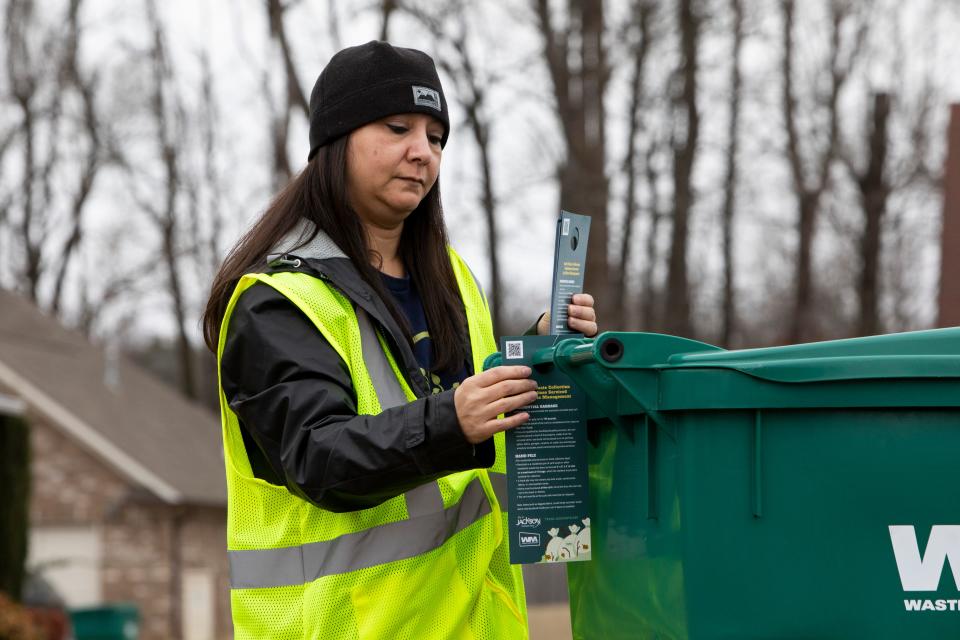 Leilani Mills, the director of health and sanitation for the city of Jackson, places flyers describing the new rule changes to bulk garbage disposal onto neighborhood garbage cans on Monday, December 12, 2022, in Jackson, Tenn. 