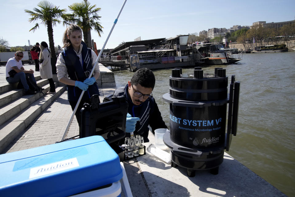 Senior technician Omar Bach-Rais takes water samples from the River Seine for analysis as Aurelie Lemaire, a microbiology research intern looks on, in Paris, Wednesday, April 5, 2023. A costly and complex clean-up is resuscitating the River Seine just in time for it to play a starring role in the 2024 Paris Olympics. The city and its region are rushing to make the Seine's murky waters swimmable, so it can genuinely live up to its billing as the world’s most romantic river. (AP Photo/Christophe Ena)