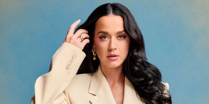 katy perry poses in a cream suit with her long hair down against a blue and yellow fade background