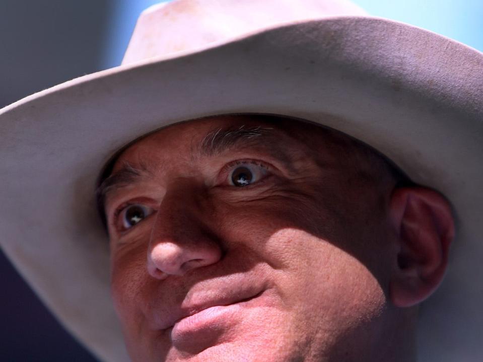 Close up ofJeff Bezos's face. he's wearing a white cowboy hat looking happy, if not slightly deranged,