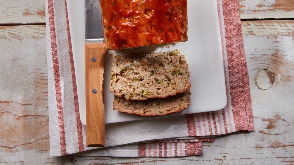 chicken meatloaf on a cutting board with a knife and a brown sugar and ketchup glaze on top