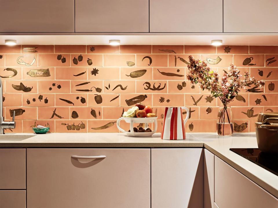 a kitchen backsplash in peach color with decorative elements like chili peppers etc with bone colored cabinets