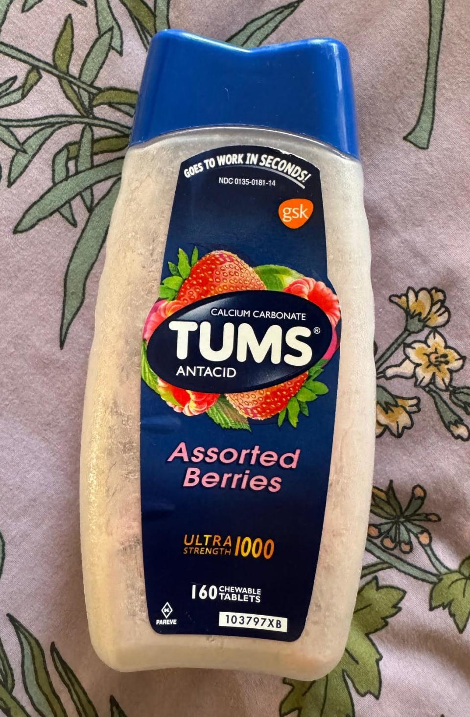 Bottle of TUMS Antacid with 'Assorted Berries' flavor lying on a floral background