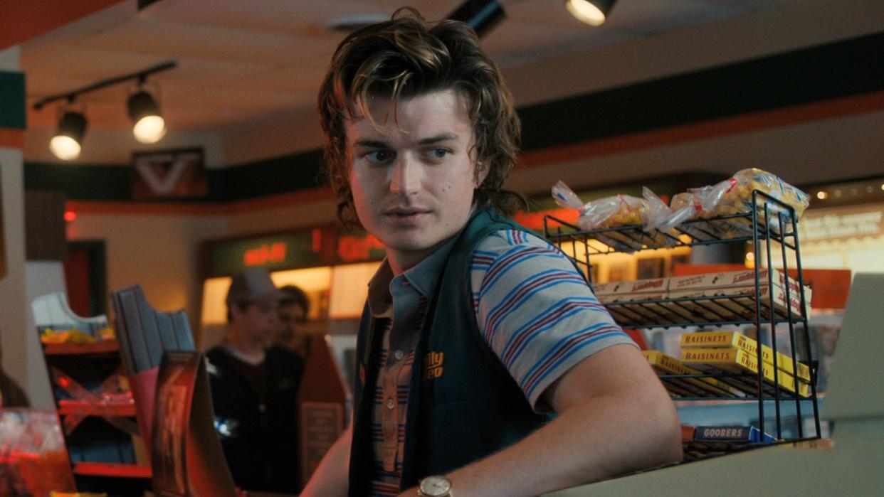  Joe Keery in Season 4 of Stranger Things leaning against a cash register. 