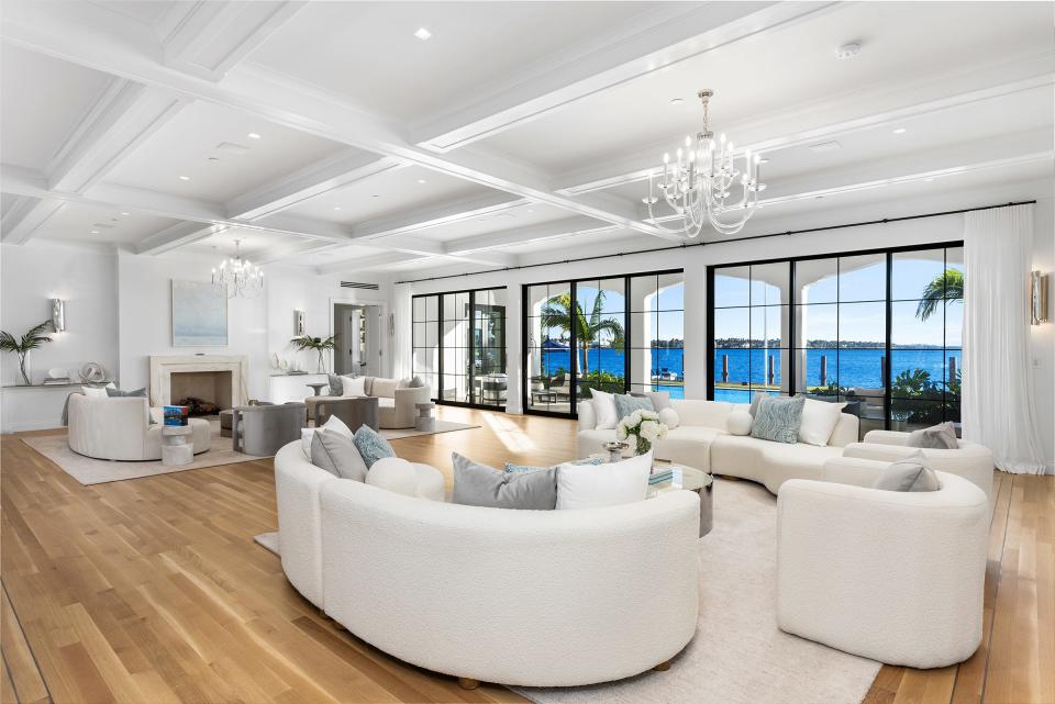 With a fireplace on one side, the main living space at 10 Tarpon Island in Palm Beach has glass doors that open onto a loggia and poolside patio with dramatic water views.