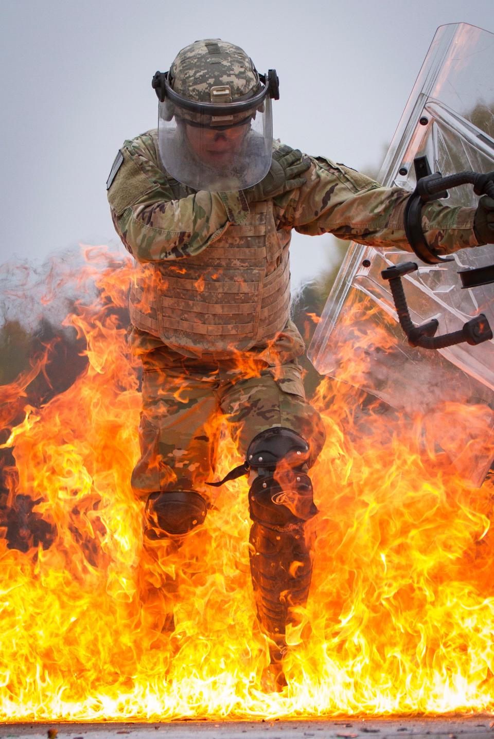 A photo of a man in riot gear batting away flames with a riot shield.