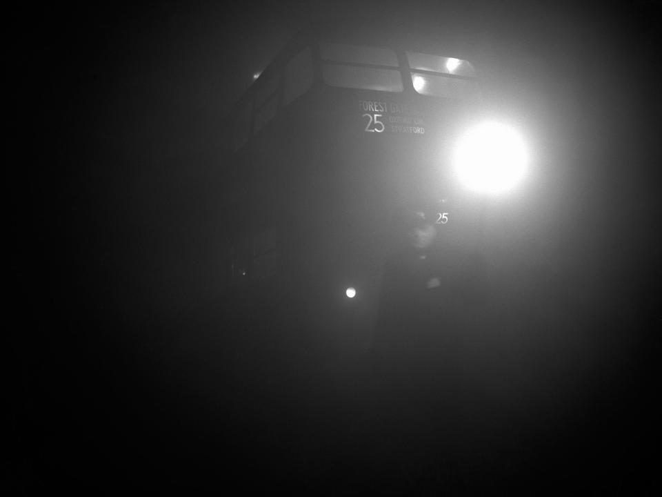 A transport inspector holding a flare leads a bus out of the terminal at Aldgate East amid dense fog in London.