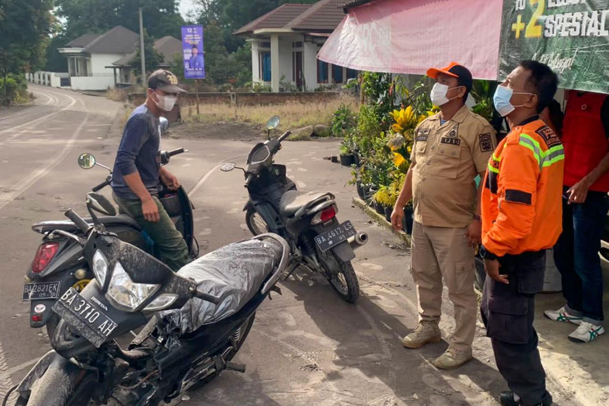 This handout picture taken and released on December 3, 2023 by Indonesia's National Disaster Agency shows officials looking on as volcanic ash from the eruption of Mount Marapi on Sumatra island covers the village of Nagari Lasi in Agam Regency. A volcano in western Indonesia erupted on December 3, belching a column of ash around three kilometres into the sky and forcing the evacuation of dozens of hikers, officials said. (