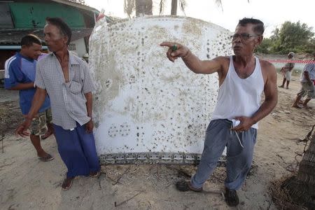 People stand next to a piece of suspected plane wreckage which has been found off the coast of southern Thailand in Nakhon Si Thammarat province, January 24, 2016. REUTERS/Surapan Boonthanom