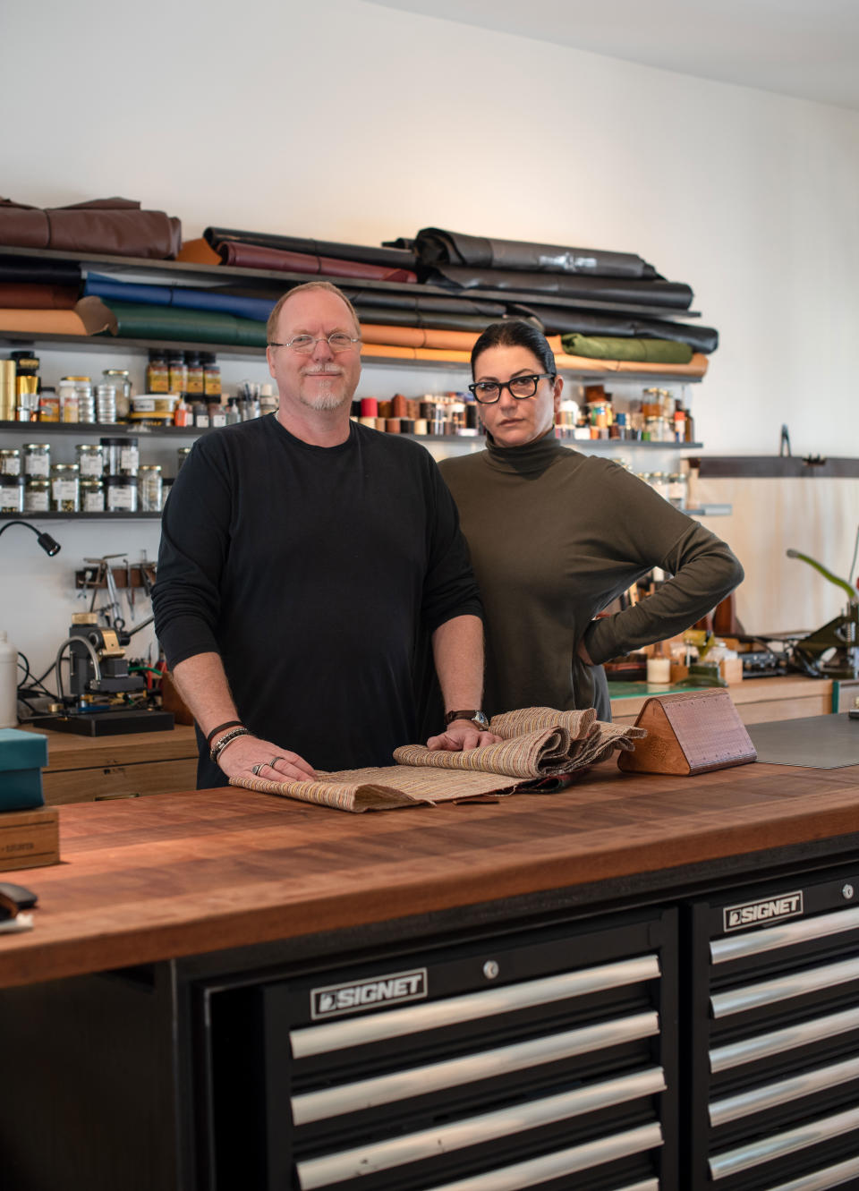 The couple pictured in Pollak’s leather-working studio. Oak shelves and cabinets were crafted by a local carpenter.