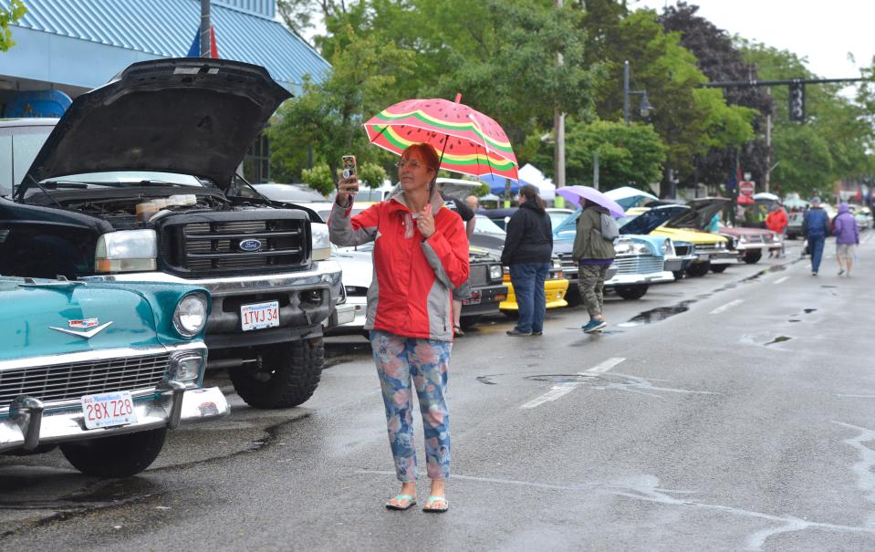 With umbrella in hand, Sandy Blajda, of West Yarmouth, takes a photo of her husband, Dan Blajda, and his 1981 Checker Cab Marathon as he wipes away the rain. The Father's Day Car Show returned last year to Main Street after a couple of years off due to the pandemic.