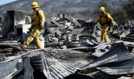 Firefighters walk over the remains of a barn destroyed by the so-called Blue Cut Fire in the San Bernardino National Forest in San Bernardino County, California, U.S. August 18, 2016. REUTERS/Gene Blevins