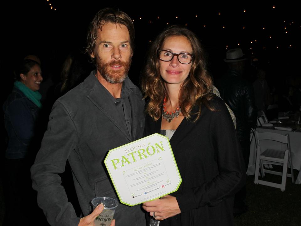 Danny Moder, in a gray suit jacket holding a drink, poses with wife Julia Roberts, in a black shirt and glasses.