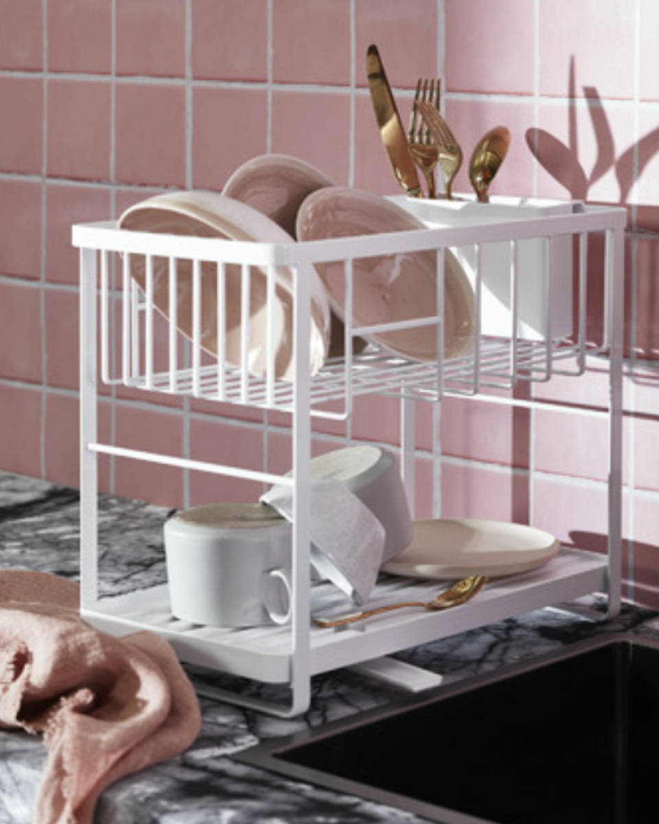 2 Level Tower Dish Drainer Rack fromTemple & Webster in white sits on a kitchen bench against pink tiles with gold cutlery and pink crockery.
