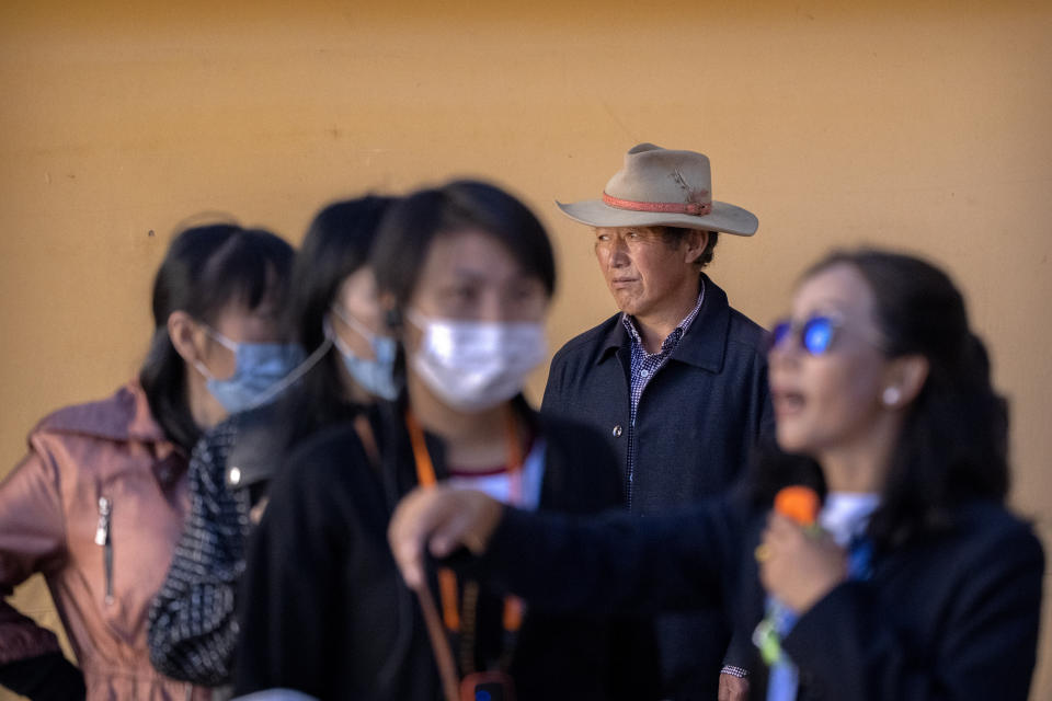 A Tibetan man stands in a courtyard as a tour guide gives a lecture to tourists at the Potala Palace in Lhasa in western China's Tibet Autonomous Region, Tuesday, June 1, 2021. Tourism is booming in Tibet as more Chinese travel in-country because of the coronavirus pandemic, posing risks to the region's fragile environment and historic sites. (AP Photo/Mark Schiefelbein)