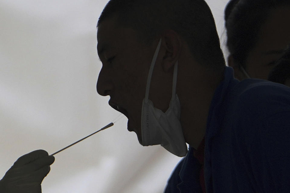 A worker has a throat swab sample taken at a coronavirus test site set up near a commercial office complex, Sunday, April 24, 2022, in Beijing. Beijing is on alert after 10 middle school students tested positive for COVID-19, in what city officials said was an initial round of testing. (AP Photo/Andy Wong)