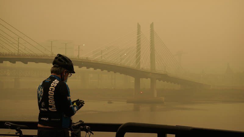 A man stops on his bike along the Willamette River as smoke from wildfires partially obscures the Tilikum Crossing Bridge, Saturday, Sept. 12, 2020, in Portland, Ore. (AP Photo/John Locher)