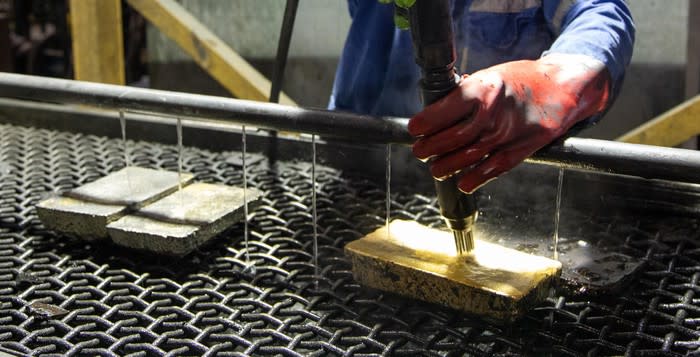 Person wearing red glove pouring ingots of precious metals.