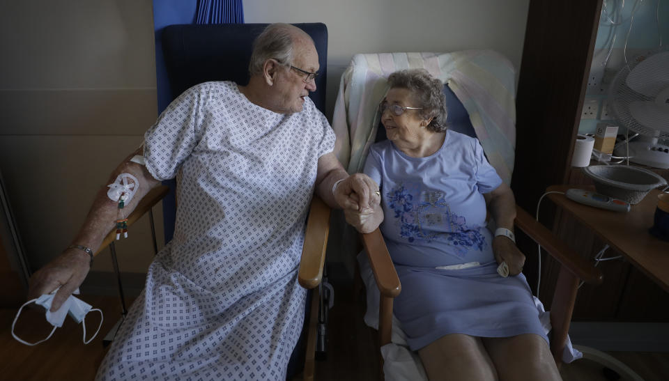 Coronavirus patients George Gilbert, 85 and his wife Domneva Gilbert 84, hold hands during a short visit, they are being treated in different areas, and both are part of the TACTIC-R trial, at Addenbrooke's hospital in Cambridge, England, Thursday, May 21, 2020. The new trial known as TACTIC-R is testing whether existing drugs will help prevent the body's immune system from overreacting, which scientists hope could prevent organ failure and death in COVID-19 patients. (AP Photo/Kirsty Wigglesworth, pool)