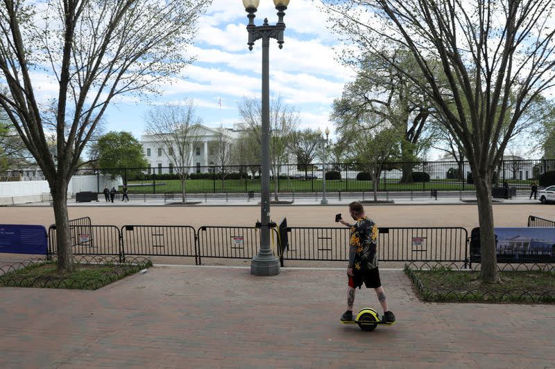 A scooter rider shoots pictures as he speeds past the empty plaza during the coronavirus outbreak, at the White House on Pennsylvania Avenue in Washington