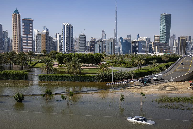 An abandoned vehicle stands in floodwater caused by heavy rain, with the Burj Khalifa, the world's tallest building, visible in the background.