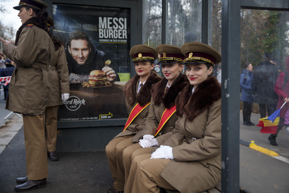 Military cadets smile while sitting in a bus stop backdropped by a billboard showing Argentinian soccer star Lionel Messi before taking part in the National Day parade in Bucharest, Romania, Friday, Dec. 1, 2023. Tens of thousands of people turned out in Romania's capital on Friday to watch a military parade that included troops from NATO allies to mark the country's National Day. (AP Photo/Vadim Ghirda)