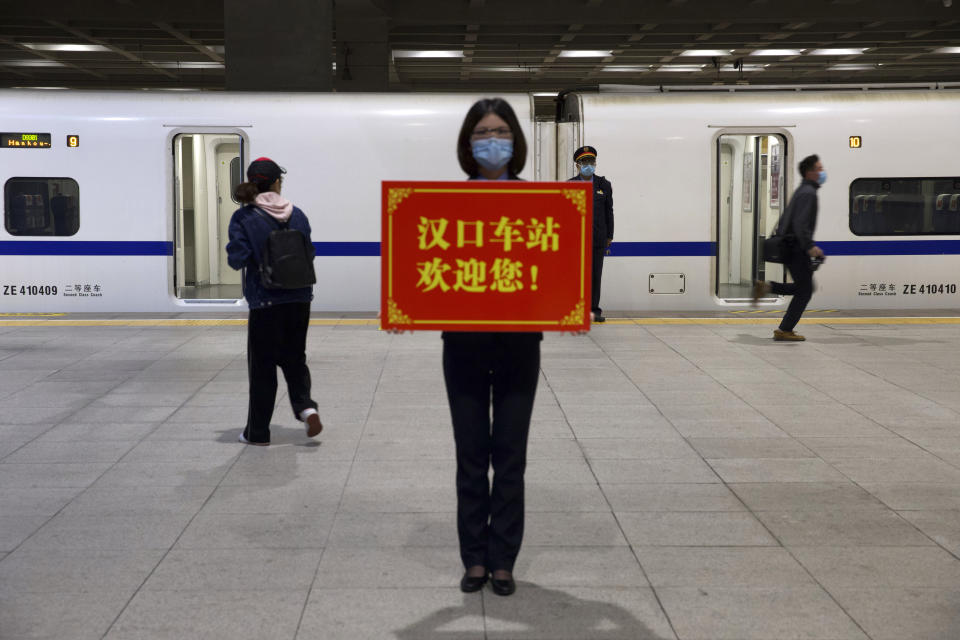 A railway worker holds a sign reading “Hankou Station welcomes you!” as passengers board the first high-speed train to leave Hankou train station after the resumption of train services in Wuhan (Ng Han Guan/AP)