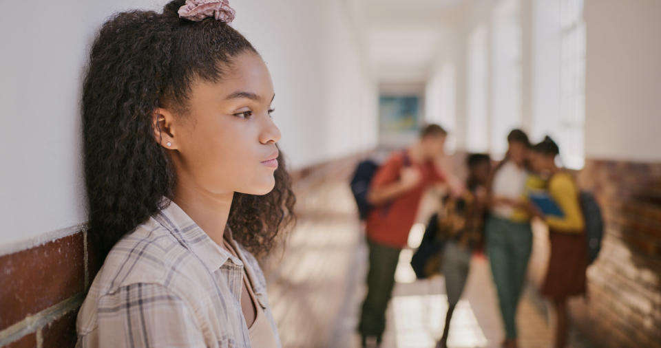 a girl alone in the hallway with people making fun of her in the background