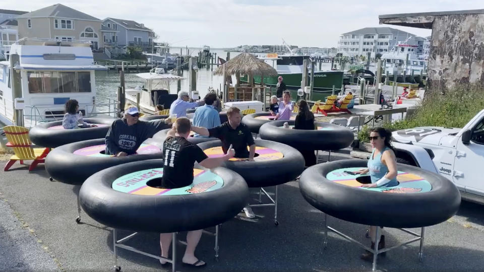 In this image made from Saturday, May 16, 2020, video provided by Revolution Event Design & Production, "bumper tables," created by the company and designed to allow people to practice social distancing while eating and talking, are debuted at Fish Tales, a restaurant in Ocean City, Md. (Katie Kirby/Revolution Event Design & Production via AP)