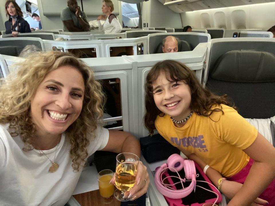 The author and her daughter on the plane on the way to Rome. The author is holding a beverage in her hand and there is an iPad connected to pink headphones between them.