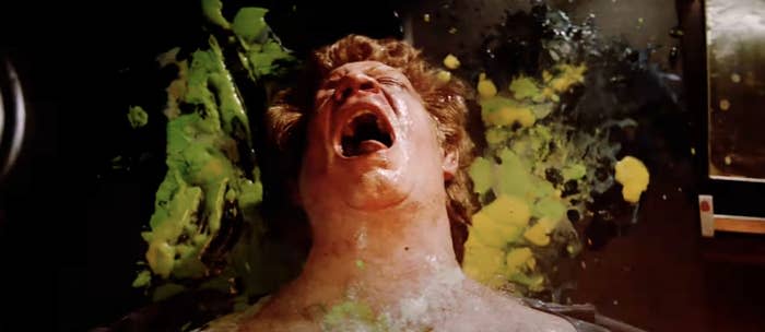 A man is screaming in apparent agony while covered in green and yellow splatters