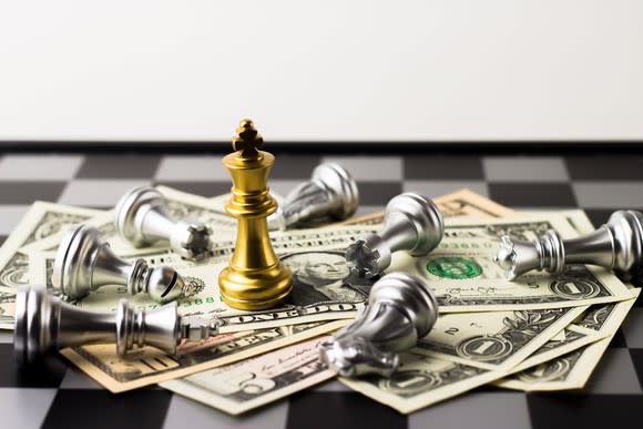 Chess pieces and cash on a chess board with king on top of cash.