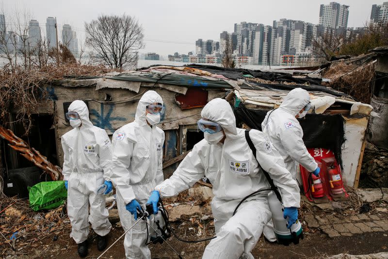 South Korean soldiers in protective gears sanitize shacks as a luxury high-rise apartment complex is seen in the background at Guryong village in Seoul