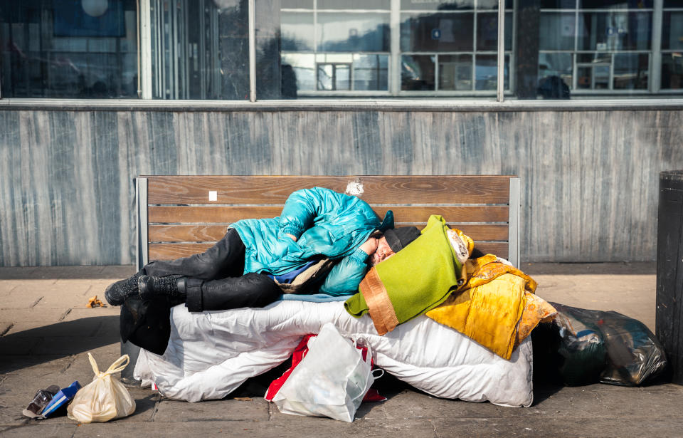 Homeless man sleep, Poor homeless man or refugee sleeping on the wooden bench on the urban street in the city with bags of clothes and junk on sunny cold day, social documentary concept