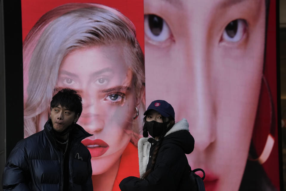 A woman wearing a mask stands near an ad featuring models for make up products in Beijing, China, Tuesday, Dec. 28, 2021. Advertisements featuring some Chinese models have sparked feuding in China over whether their appearance and makeup are perpetuating harmful stereotypes of Asians. (AP Photo/Ng Han Guan)