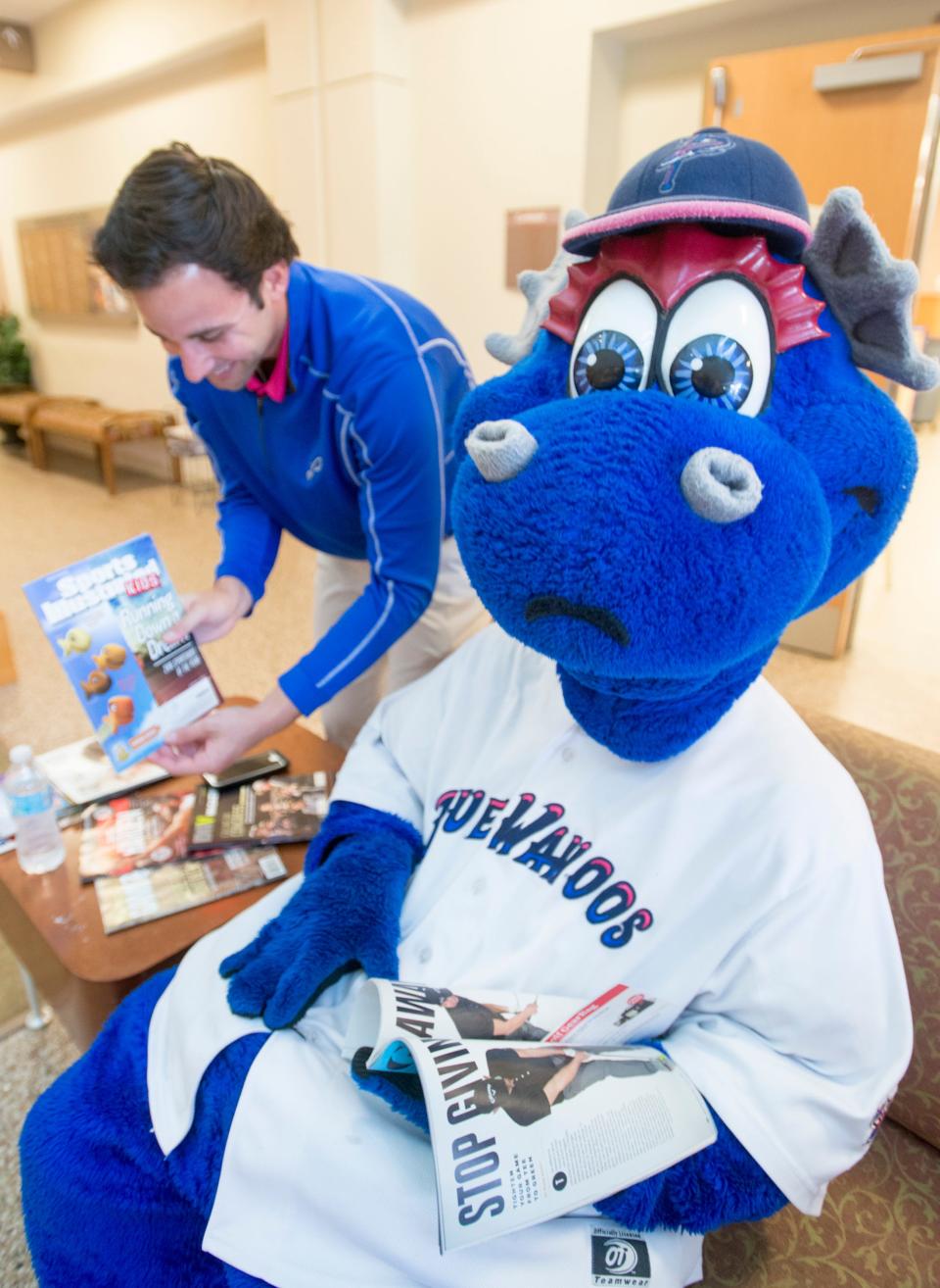 Blue Wahoos mascot Kazoo reacts to Chris Garagiola showing him a magazine cover with golfish while visiting the Gulf Coast Veterans Health Care System - Joint Ambulatory Care Center: Outpatient Clinic in honor of Armed Forces Day in Pensacola on Friday, May 19, 2017.