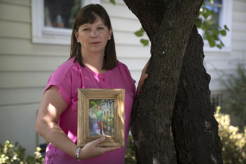 Jessica Riester Hart stands near a sweetgum tree in her yard that her daughter Allie liked to climb as she holds a photo of her daughter, Thursday, Sept. 14, 2023, in Washington. 5-year-old Allie Hart was struck and killed in 2021 by a driver while riding her bicycle in a crosswalk near their home. (AP Photo/Mark Schiefelbein)