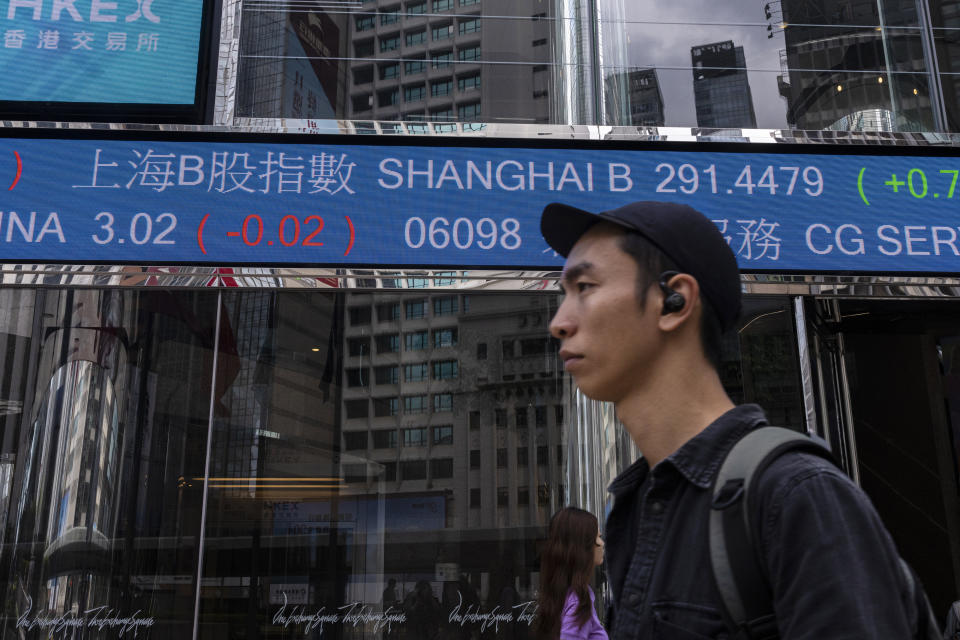 A pedestrian passes by the Hong Kong Stock Exchange electronic screen in Hong Kong, Friday, March 24, 2023. (AP Photo/Louise Delmotte)