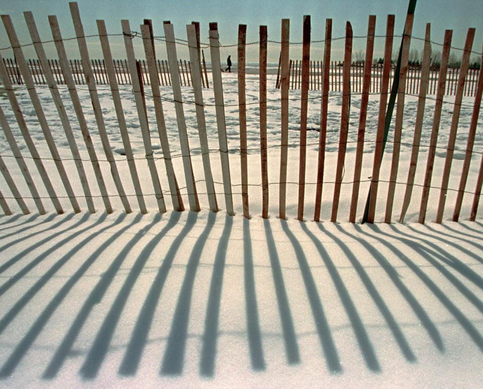 A snowfence casts long shadows in the bright sunshine as a man walks along Kew Beach in Toronto on March 25.