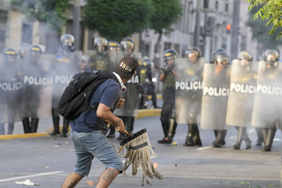 An anti-government protester holding a mop faces police in Lima, Peru, Tuesday, Jan. 24, 2023. Protesters are seeking the resignation of President Dina Boluarte, the release from prison of ousted President Pedro Castillo, immediate elections and justice for demonstrators killed in clashes with police. (AP Photo/Martin Mejia)