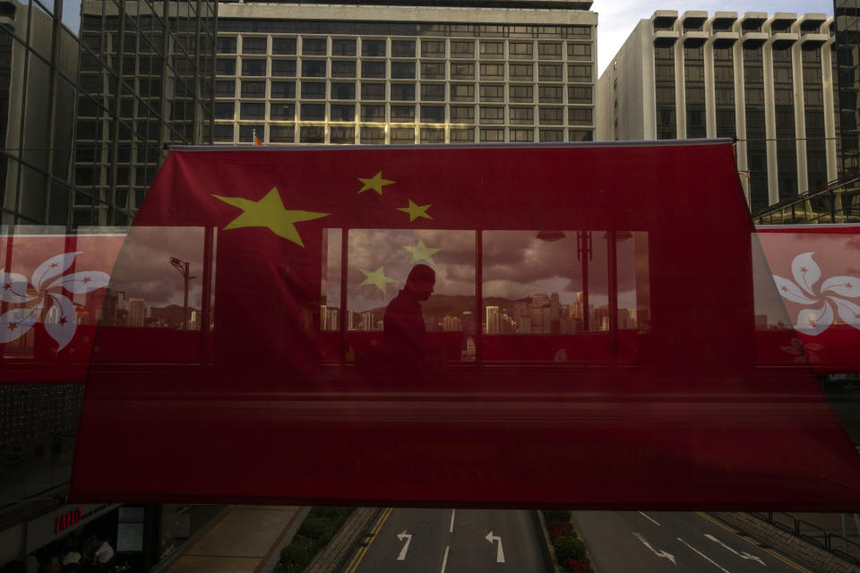 FILE- A pedestrian walks through a footbridge is silhouetted as Chinese and Hong Kong flags are strung to mark the 26th anniversary of the city's handover from Britain to China in Hong Kong, on June 27, 2023. Hong Kong’s plan to enact a new national security law, on top of a sweeping legislation that was imposed by Beijing and used to crack down on dissent, is deepening concerns over the erosion of freedoms in the former British colony.(AP Photo/Louise Delmotte, File)