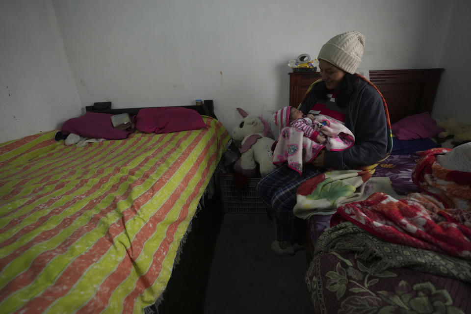 La madre soltera Tania Herrera sostiene a su hija de 20 días de nacida, Sara Milena, mientras se alimenta de lactancia materna en la única habitación de la choza en la que vive con sus padres en Quito, Ecuador, el lunes 15 de noviembre de 2022. Los padres de Herrera son el sustento familiar y ganan entre cinco y siete dólares diarios con los que alimentar a cinco adultos y mantener a la recién llegada. Esos ingresos apenas alcanzan para dos comidas al días para los adultos: café con pan, cuando hay, por la mañana y un plato de arroz por la noche, o puede que no. (AP Foto/Dolores Ochoa)