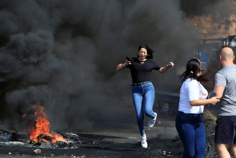 A bystander makes her way through burning tires during a protest targeting the government over an economic crisis, at Barja