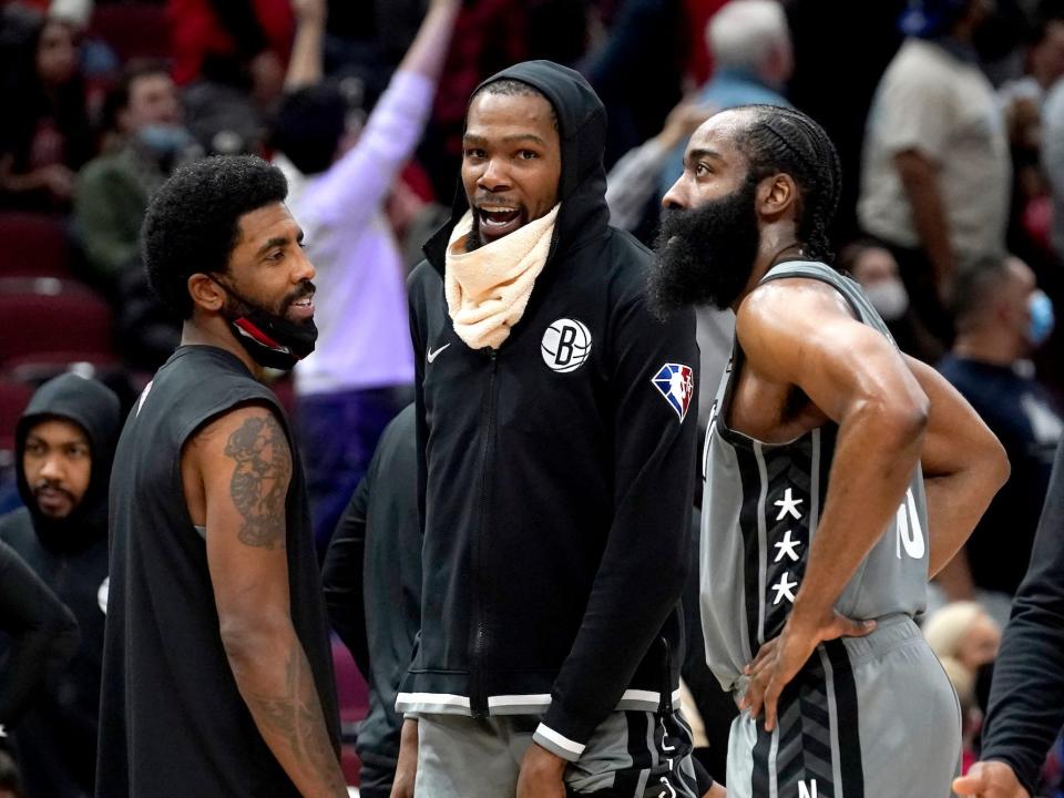 Kyrie Irving, Kevin Durant, and James Harden stand in a circle, smiling and talking during a Nets game in 2021.