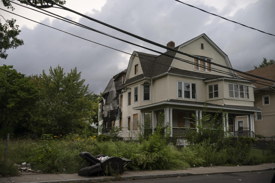 A discarded reclining chair is left on the sidewalk of a residential street in front of a house with a damaged facade in Hartford, Conn., on Tuesday Sept. 13, 2022. A majority of Black residents in Hartford are renters who live in old houses, often suffering from issues like mold and asbestos, which exacerbate health conditions like asthma, particularly for children. (AP Photo/Wong Maye-E)