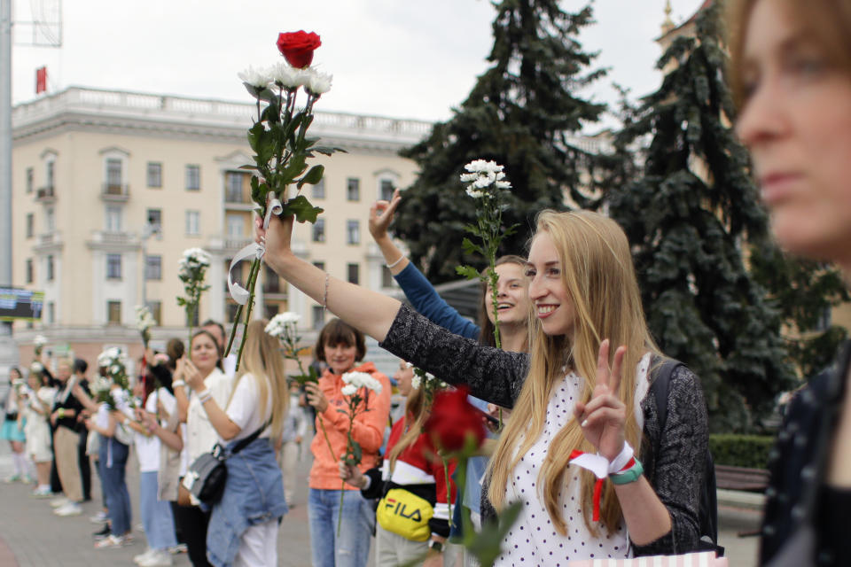 Belarusian opposition supporters hold flowers and flash victory signs during a protest in Victory Square in Minsk, Belarus, Thursday, Aug. 20, 2020. Demonstrators are taking to the streets of the Belarusian capital and other cities, keeping up their push for the resignation of the nation's authoritarian leader. President Alexander Lukashenko has extended his 26-year rule in a vote the opposition saw as rigged. (AP Photo/Sergei Grits)