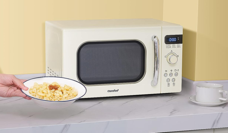the cream-colored comfee microwave on a counter next to someone's hand holding a bowl of popcorn