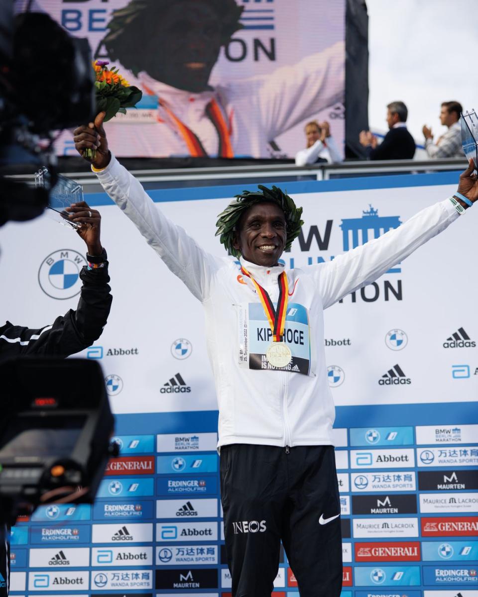 kipchoge wearing gold medal and holding bouquet on podium of berlin marathon