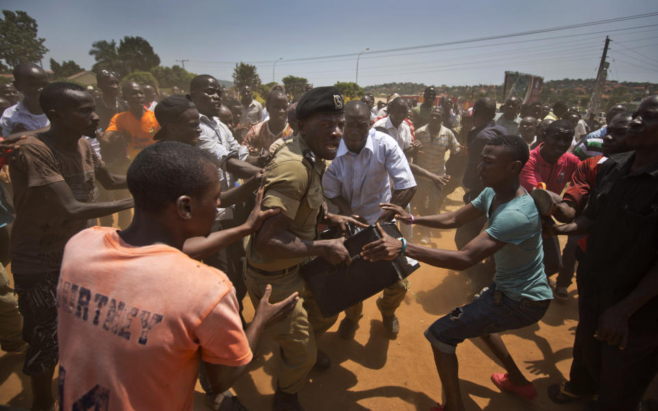 FILE - In this Feb. 18, 2016 file photo, a police officer struggles to keep hold of a box containing voting material as excited voters surround him after waiting over 7 hours without being able to vote, at a polling station in Ggaba, on the outskirts of Kampala, Uganda. On Friday, Jan. 15, 2021, The Associated Press reported on this photo circulating online incorrectly asserting it shows young people in Uganda stopping a policeman from stealing a ballot box during the country’s presidential election on Thursday. The photo was taken during Uganda’s last presidential election in 2016. (AP Photo/Ben Curtis, File)