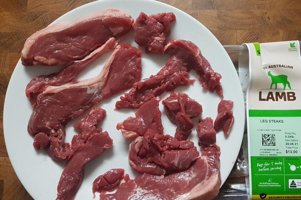 Strips of lamb steaks sit on a plate next to Woolworths packaging.